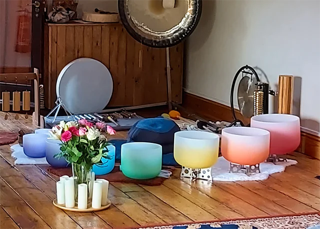 Crystal singing bowls, flowers, candles and a gong arranged on a wooden floor before a session