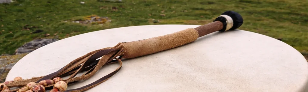 A suede-covered beater with leather tassels lying across a hide drum, out on the moor